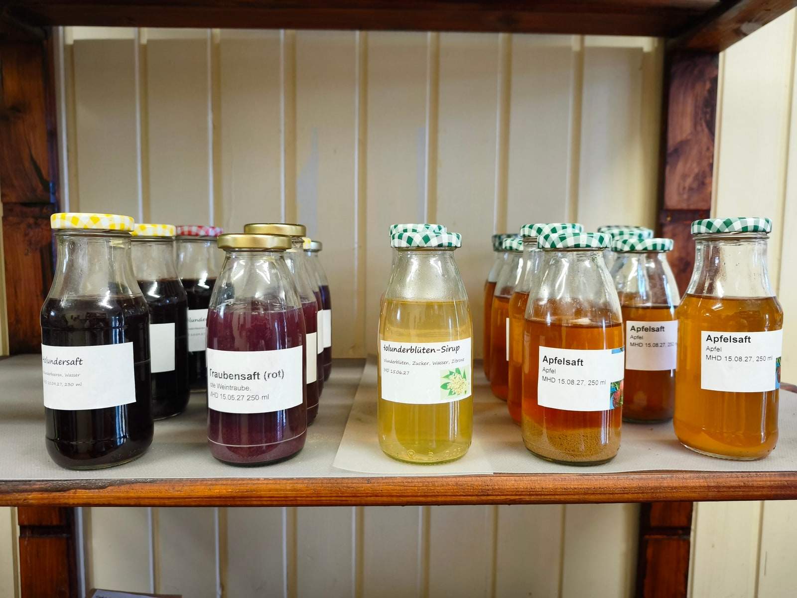 Sieben Saftflaschen stehen in einer Reihe auf einem Brett im Verkaufswagen, von fast schwarzem Holundersaft über roten Traubensaft und hellen Holunderblütensirup bis zu goldgelbem Apfelsaft.